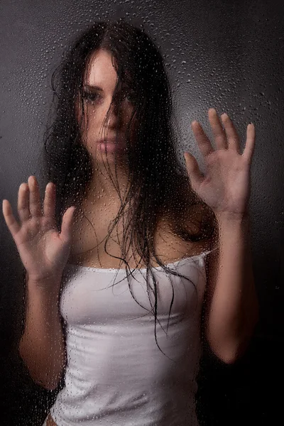 stock image A beautiful girl in a white t-shirt, on a black background behind the glass.