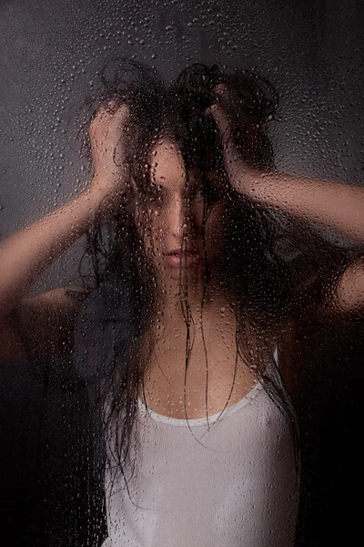 stock image A beautiful girl in a white t-shirt, on a black background behind the glass.